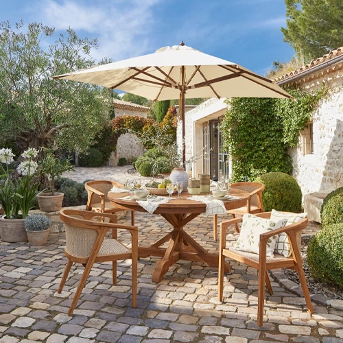 Tavolo da giardino in legno con ombrellone e quattro sedie su pavimento in pietra in patio soleggiato
