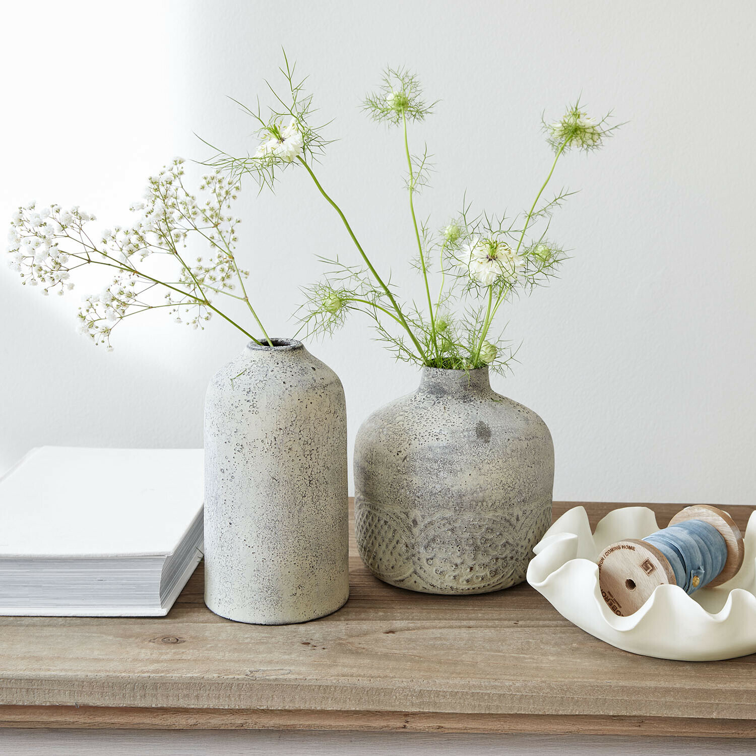 Due vasi in ceramica grigia con fiori bianchi delicati su un tavolo in legno chiaro