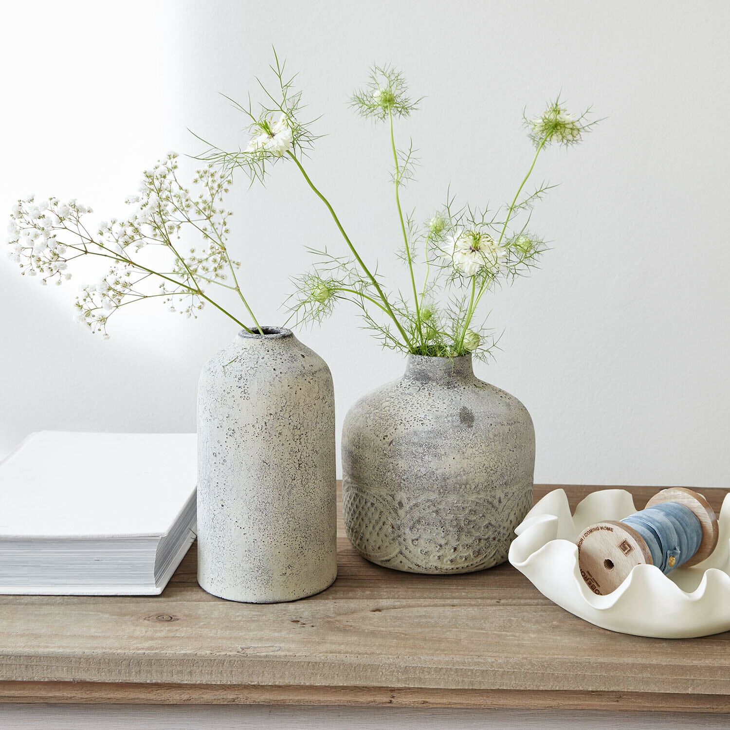 Due vasi in ceramica grigia con fiori bianchi delicati su un tavolo in legno chiaro