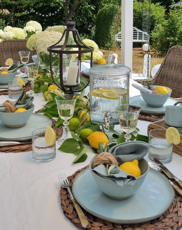 Tavola estiva all'aperto con ceramica azzurra, limoni e caraffa di vetro con acqua al limone