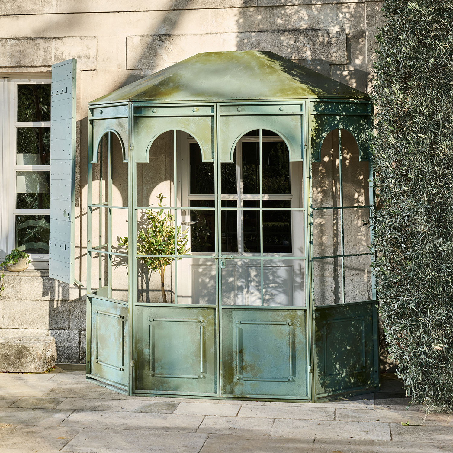 Gazebo da giardino in metallo verde con pannelli in vetro e archi decorativi su terrazza in pietra