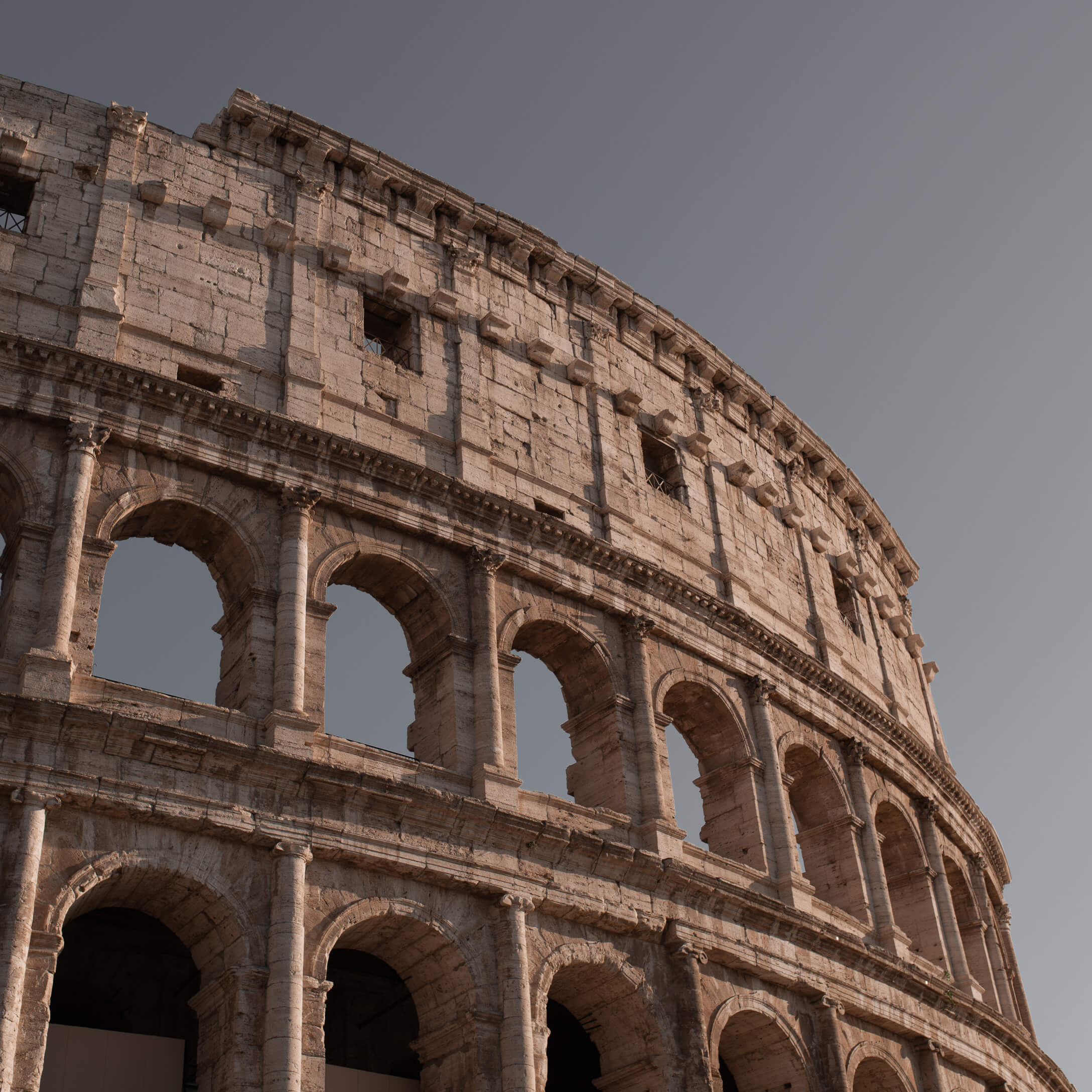 Dettaglio del Colosseo romano antico in pietra calda sotto un cielo azzurro