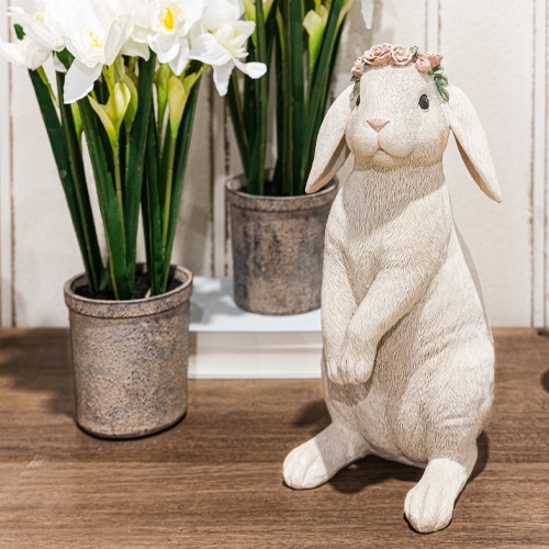 Coniglio decorativo bianco con corona di fiori su tavolo in legno accanto a vasi con fiori bianchi