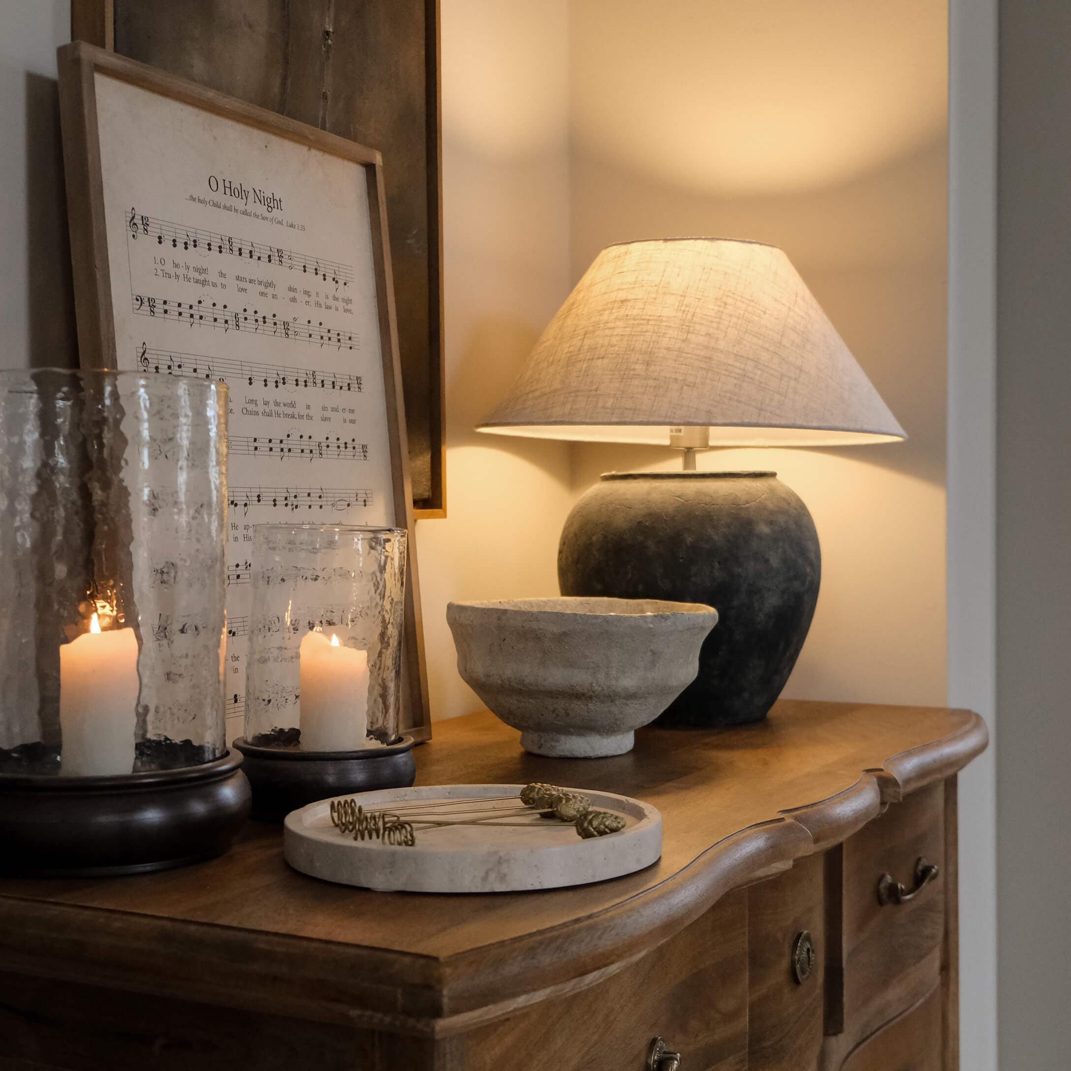 Lampada da tavolo con base in ceramica nera e paralume beige su comò in legno con decorazioni