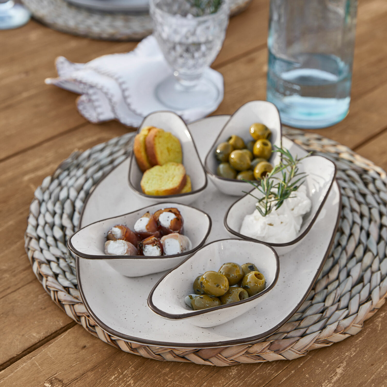 Set di 6 ciotoline su piatto Biarré Ciotole in ceramica bianca con olive e formaggio su sottopentola intrecciato su tavolo in legno