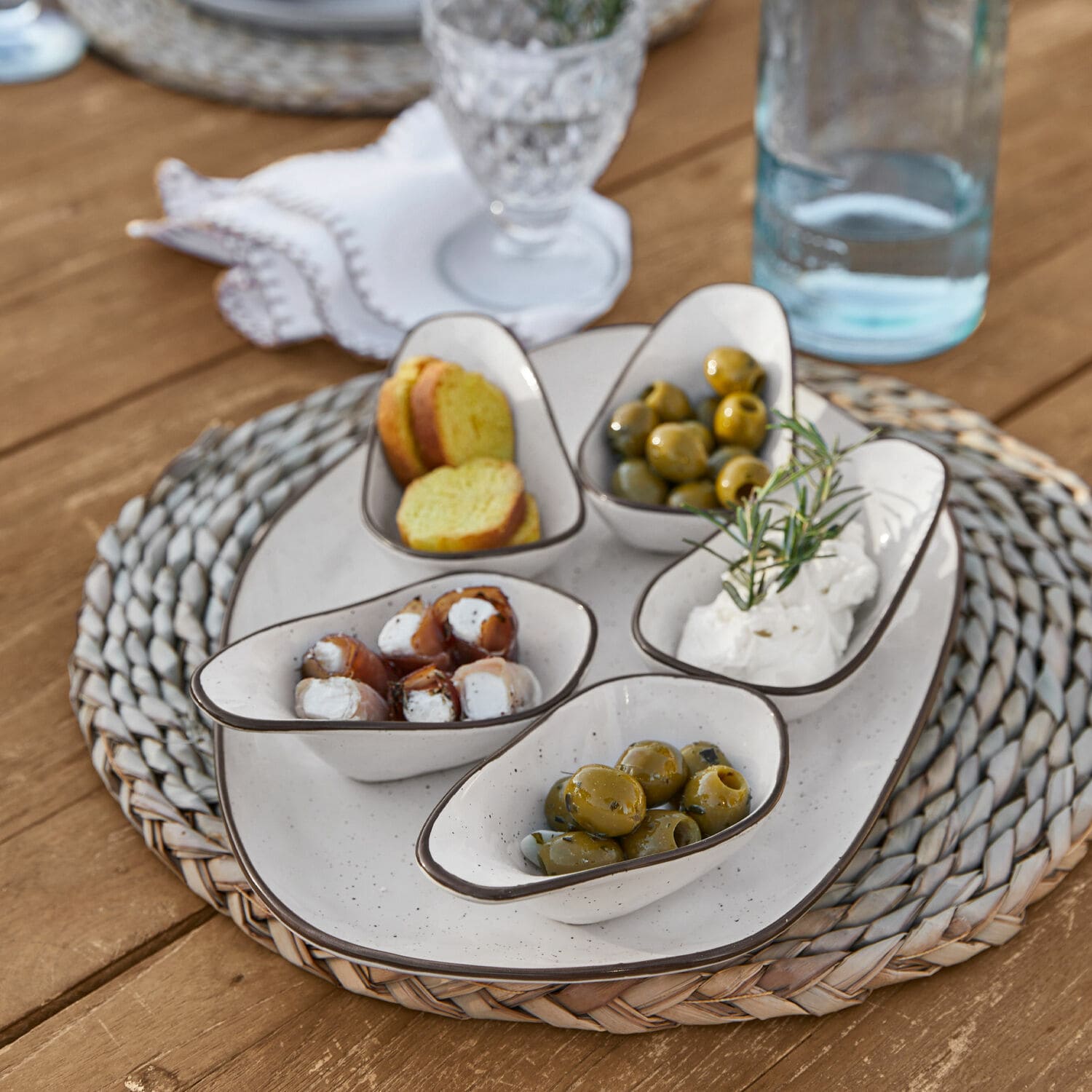 Set di 6 ciotoline su piatto Biarré Ciotole in ceramica bianca con olive e formaggio su sottopentola intrecciato su tavolo in legno