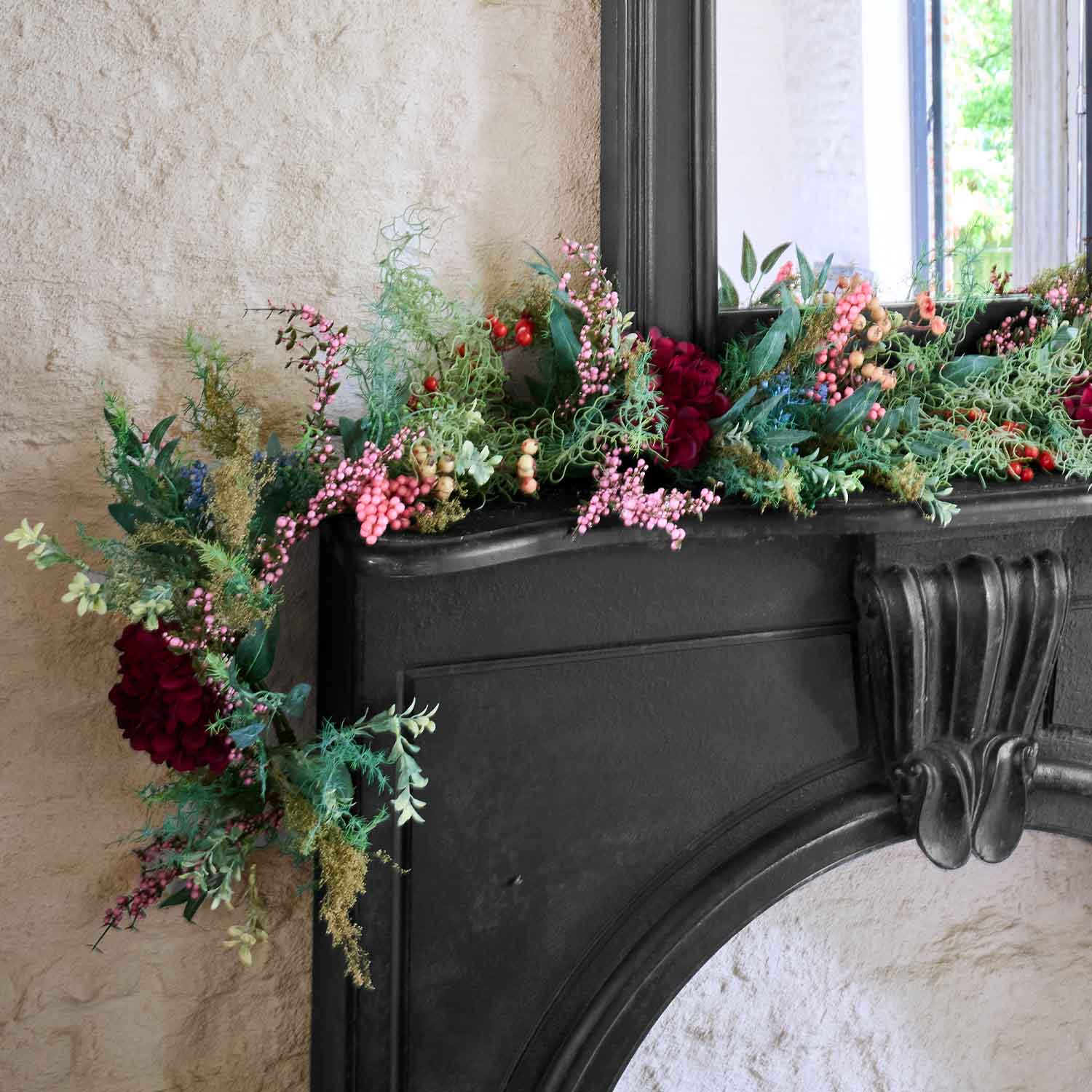Ghirlanda decorativa con bacche rosse e rosa e foglie verdi su camino nero