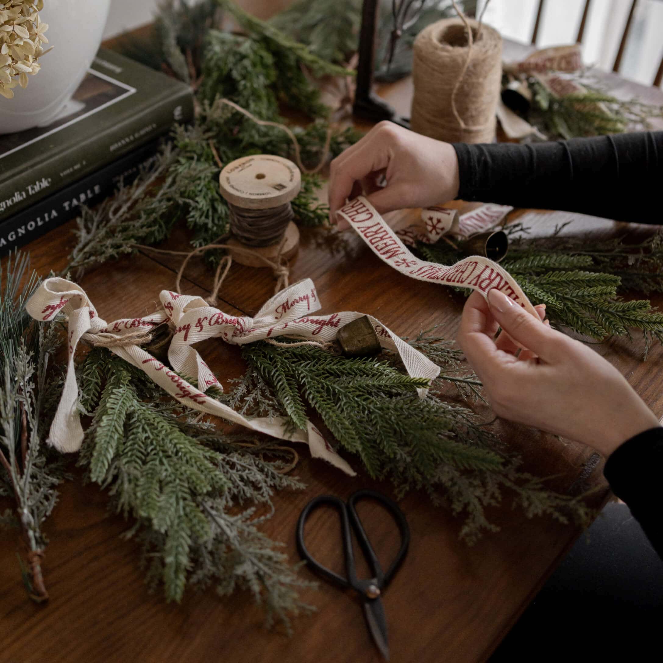 Mani che decorano rami verdi con nastro di cotone Merry Christmas su tavolo di legno con forbici