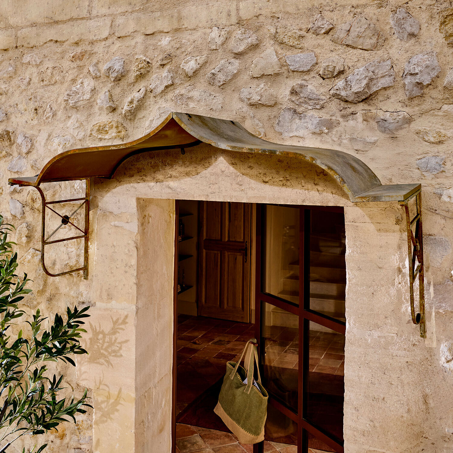 Pensilina in metallo rustico sopra ingresso con muro in pietra, protezione dalla pioggia