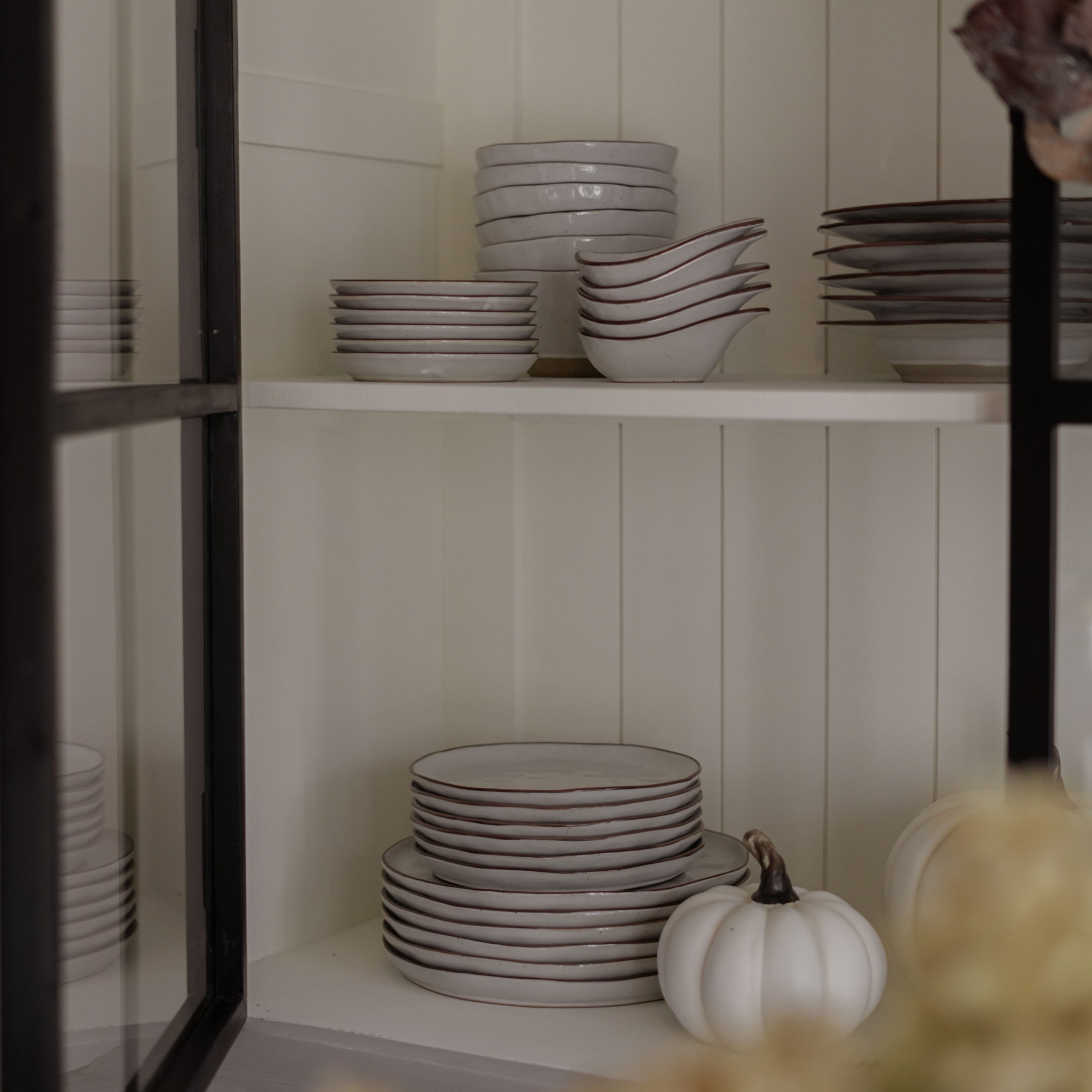 Set di ceramica bianca con bordo marrone su mensola, zucca bianca decorativa accanto, stile rustico