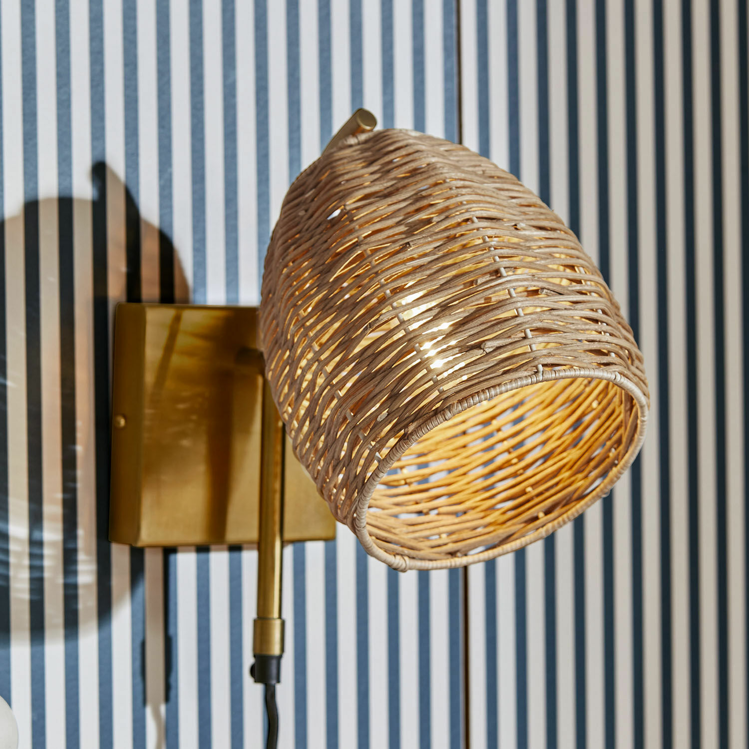 Lampada da parete Anglemont Applique con paralume in rattan intrecciato e base in ottone su sfondo a righe