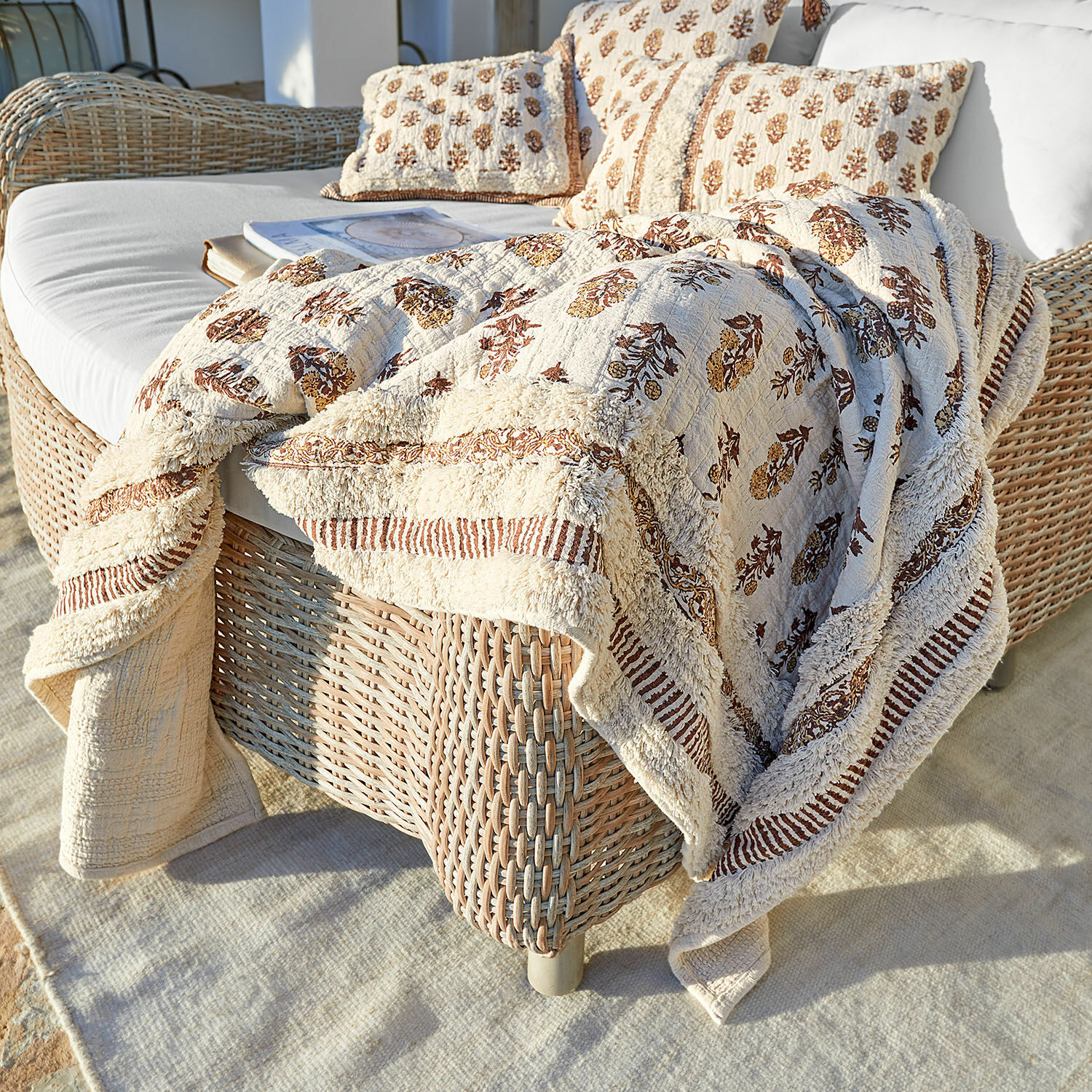 Plaid Arsalan Coperta e cuscini in cotone beige con motivo marrone su divano in vimini in terrazza