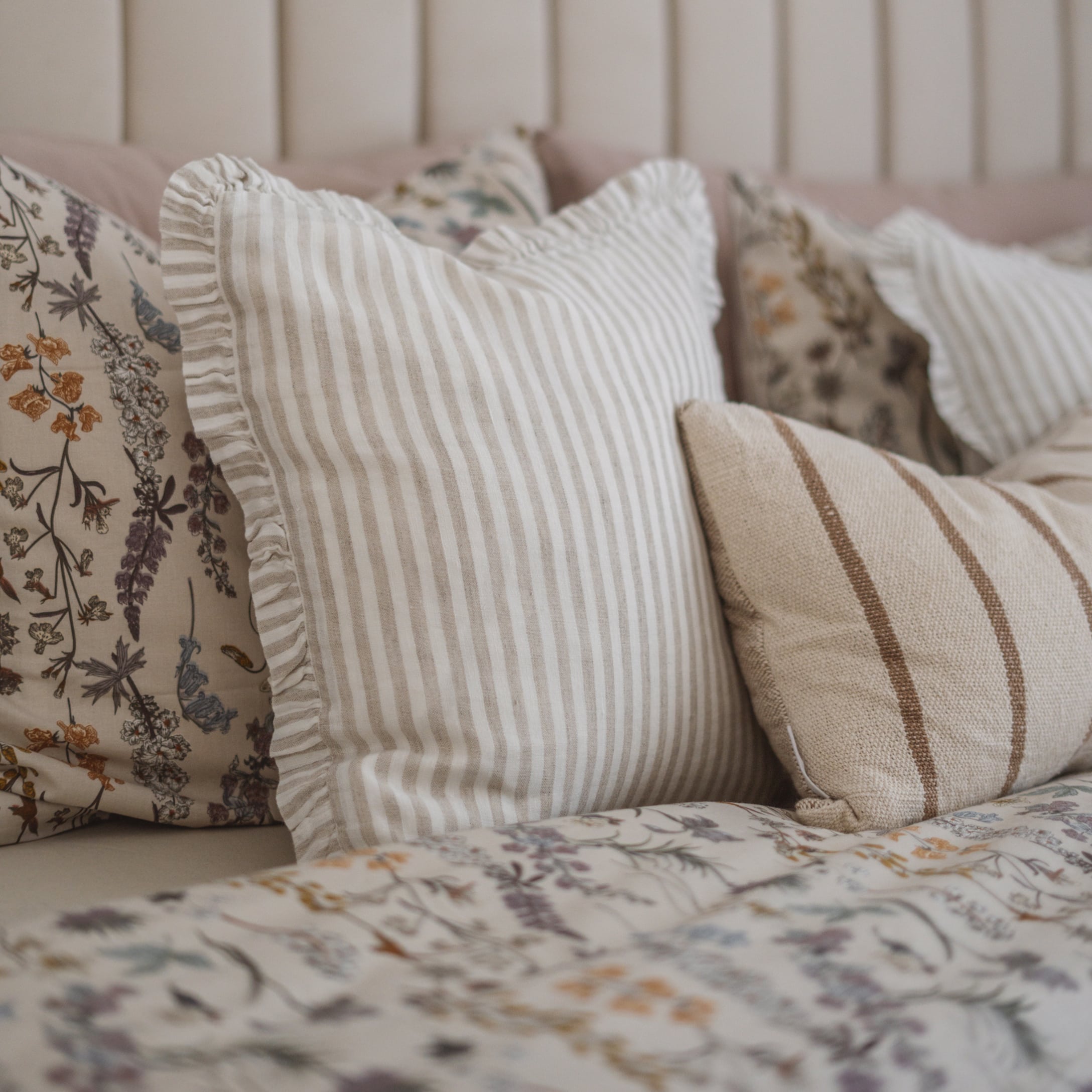 Set di cuscini decorativi a righe beige e motivo floreale su letto in camera da letto