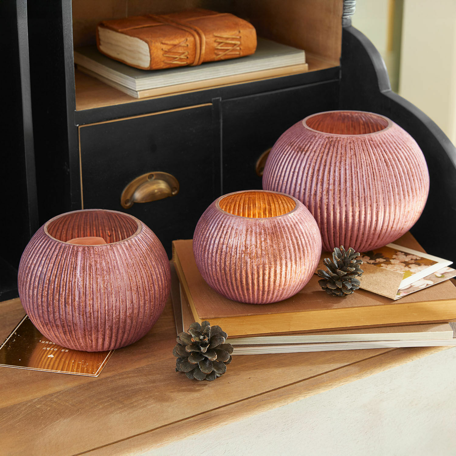 Set di 3 portalumini Jalimeen Set di tre portacandele in vetro rosa rigato su tavolo in legno con decorazioni naturali