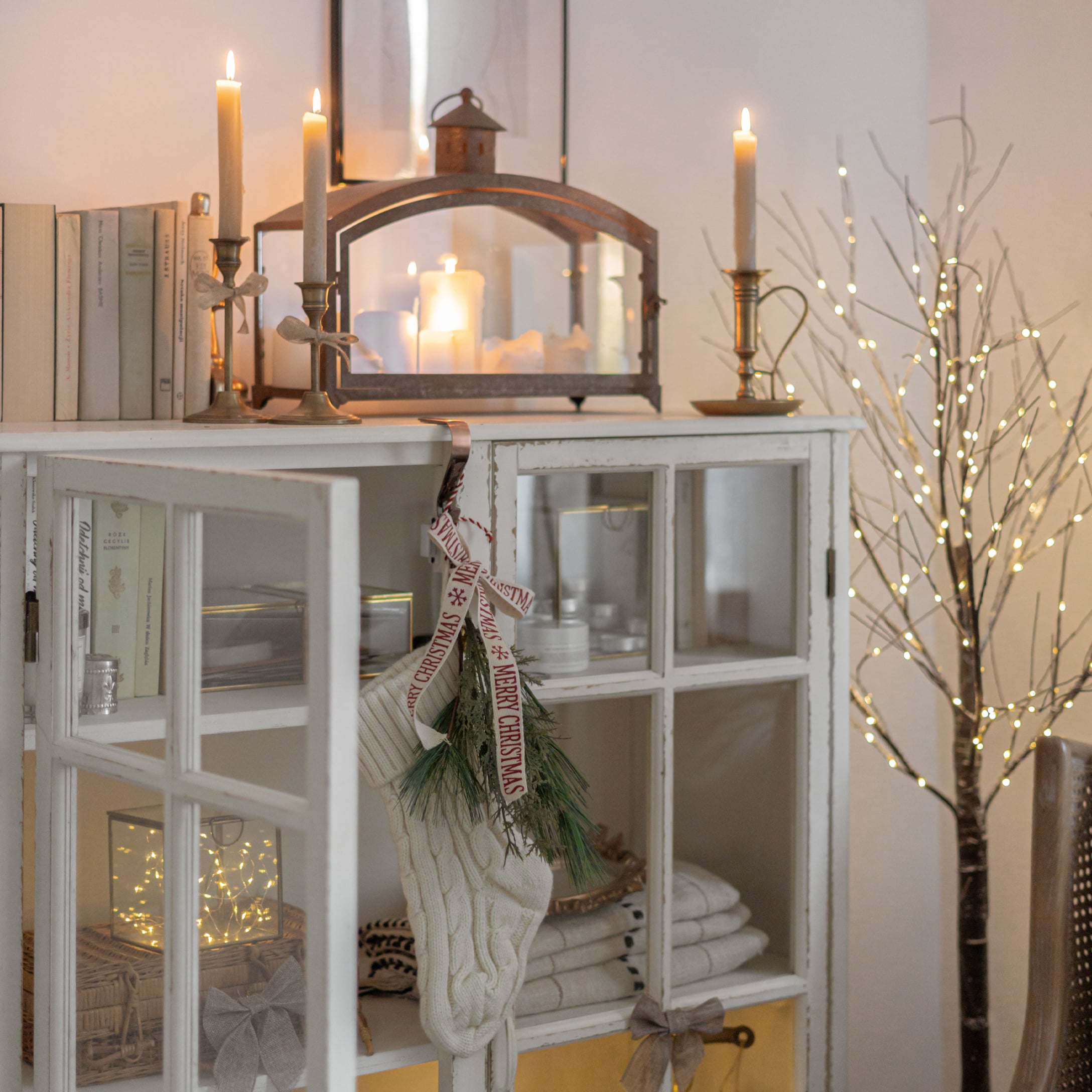 Mobile bianco con porta in vetro, calza natalizia e candelabri per decorazione festiva