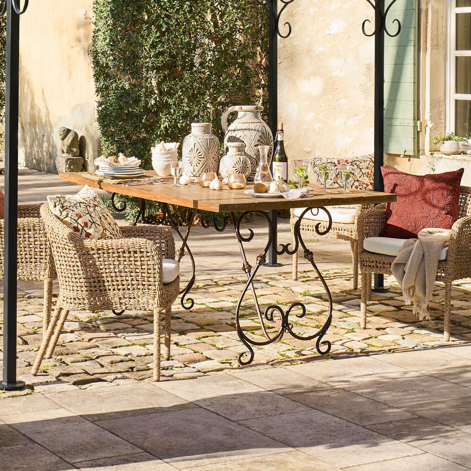 Tavolo da giardino con piano in legno e gambe in metallo, sedie in vimini con cuscini e decorazioni in ceramica