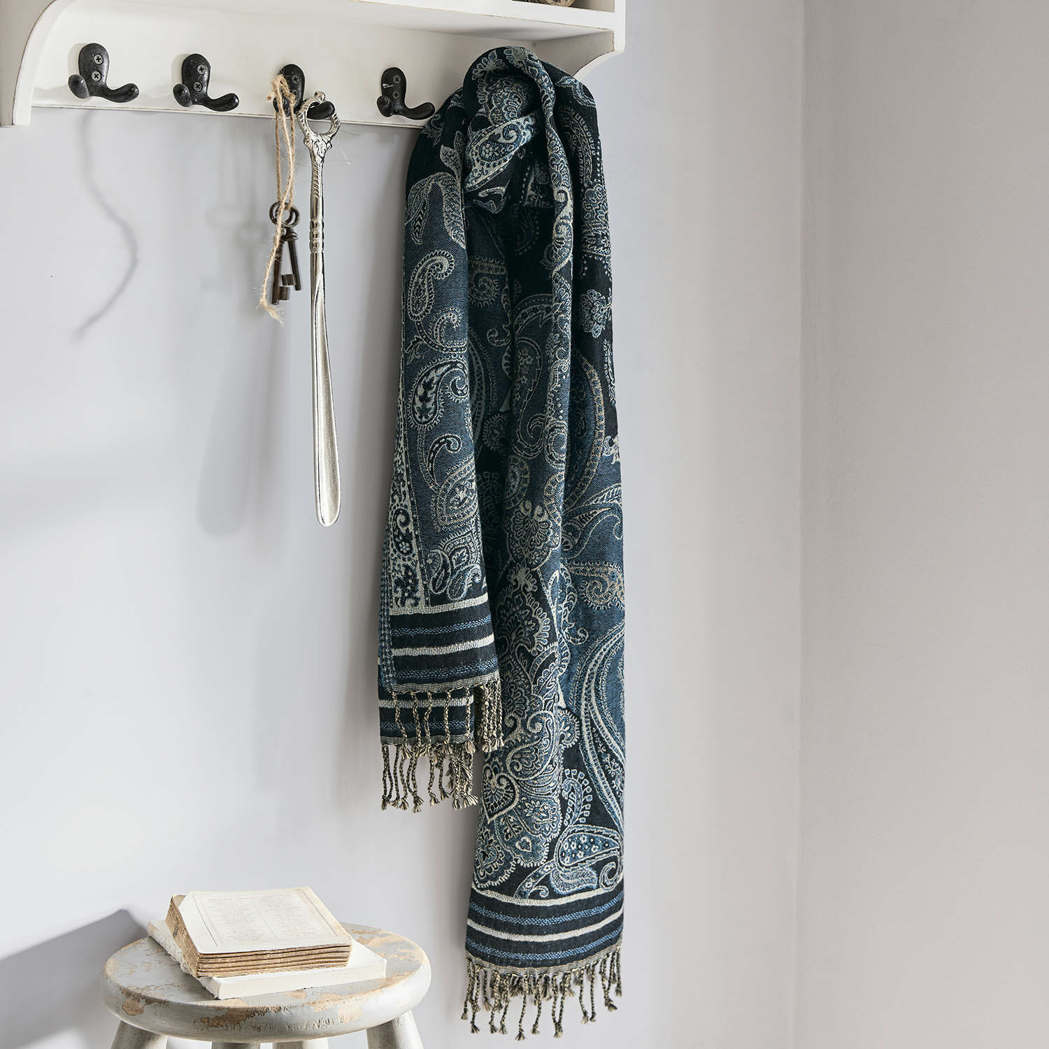 Sciarpa Eloas Sciarpa blu scuro con motivo paisley e frange appesa a appendiabiti bianco in ambiente luminoso