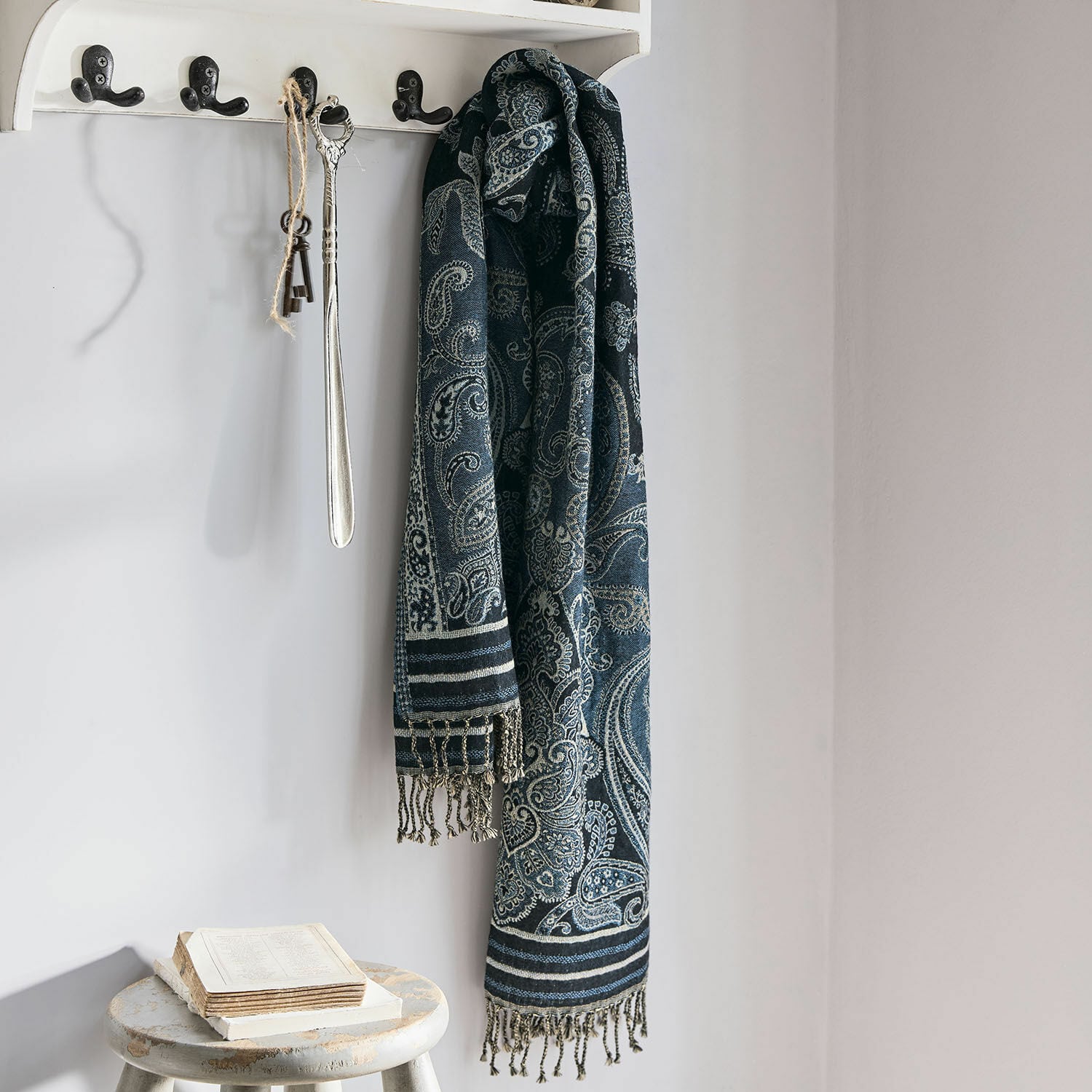 Sciarpa Eloas Sciarpa blu scuro con motivo paisley e frange appesa a appendiabiti bianco in ambiente luminoso