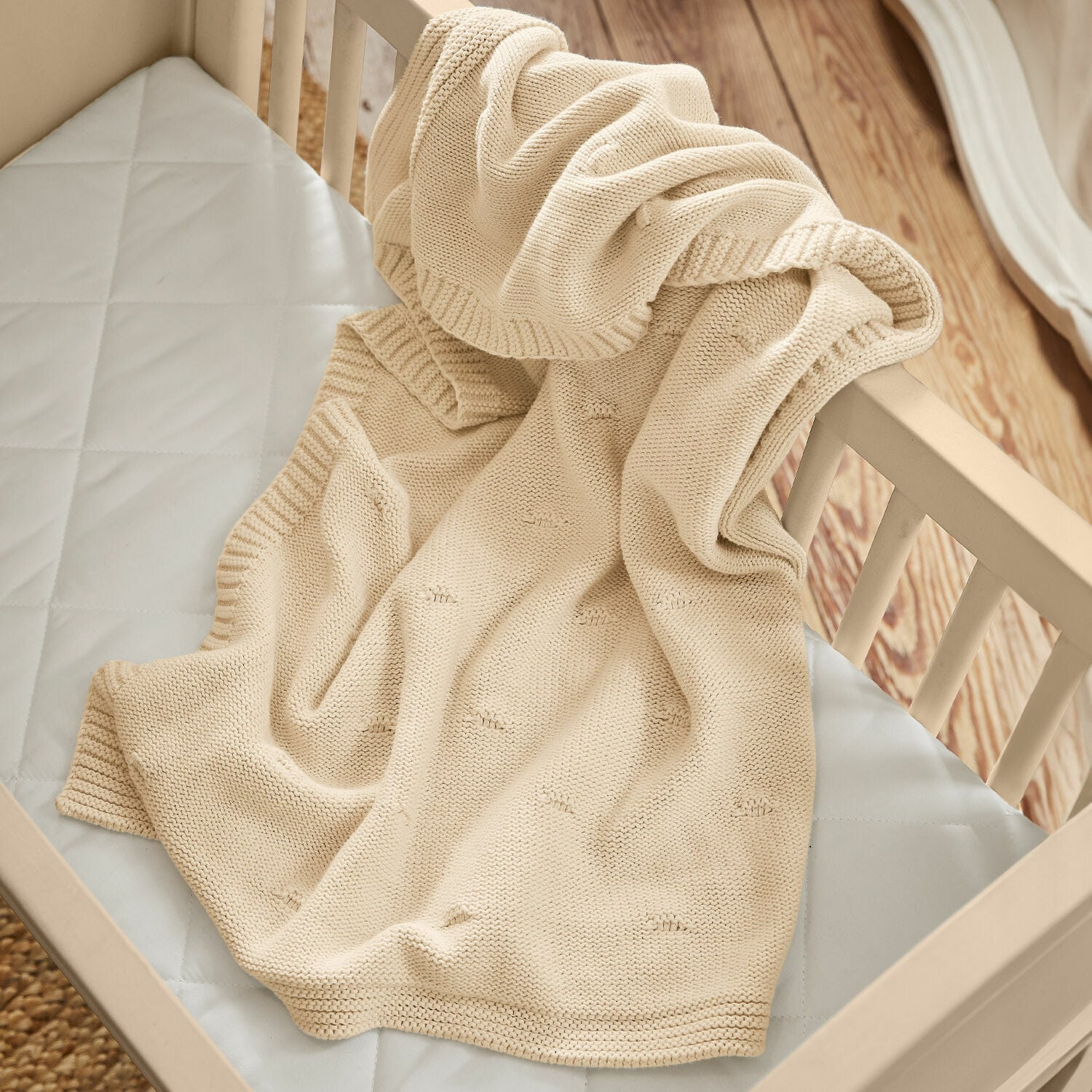 Coperta Samiya Coperta beige in cotone lavorata a maglia su lettino in legno chiaro, morbida e accogliente