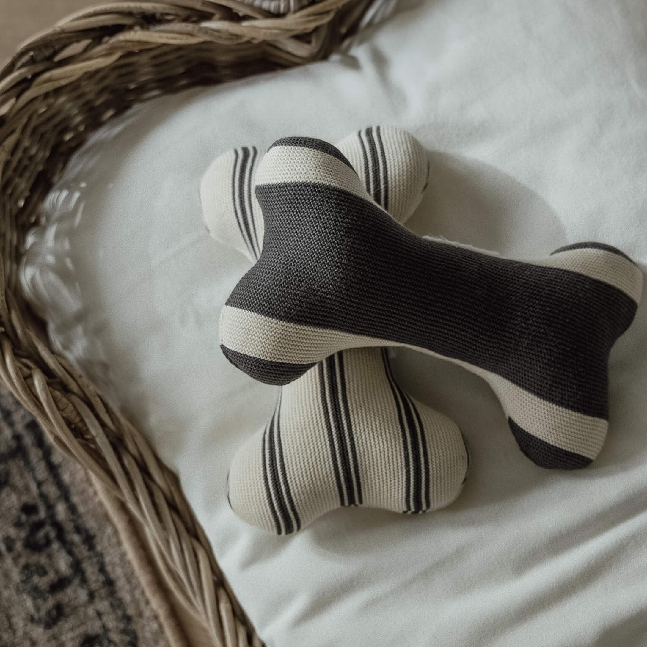 Due giocattoli a forma di osso in maglia a righe bianco e nero su sfondo bianco in cesto di vimini