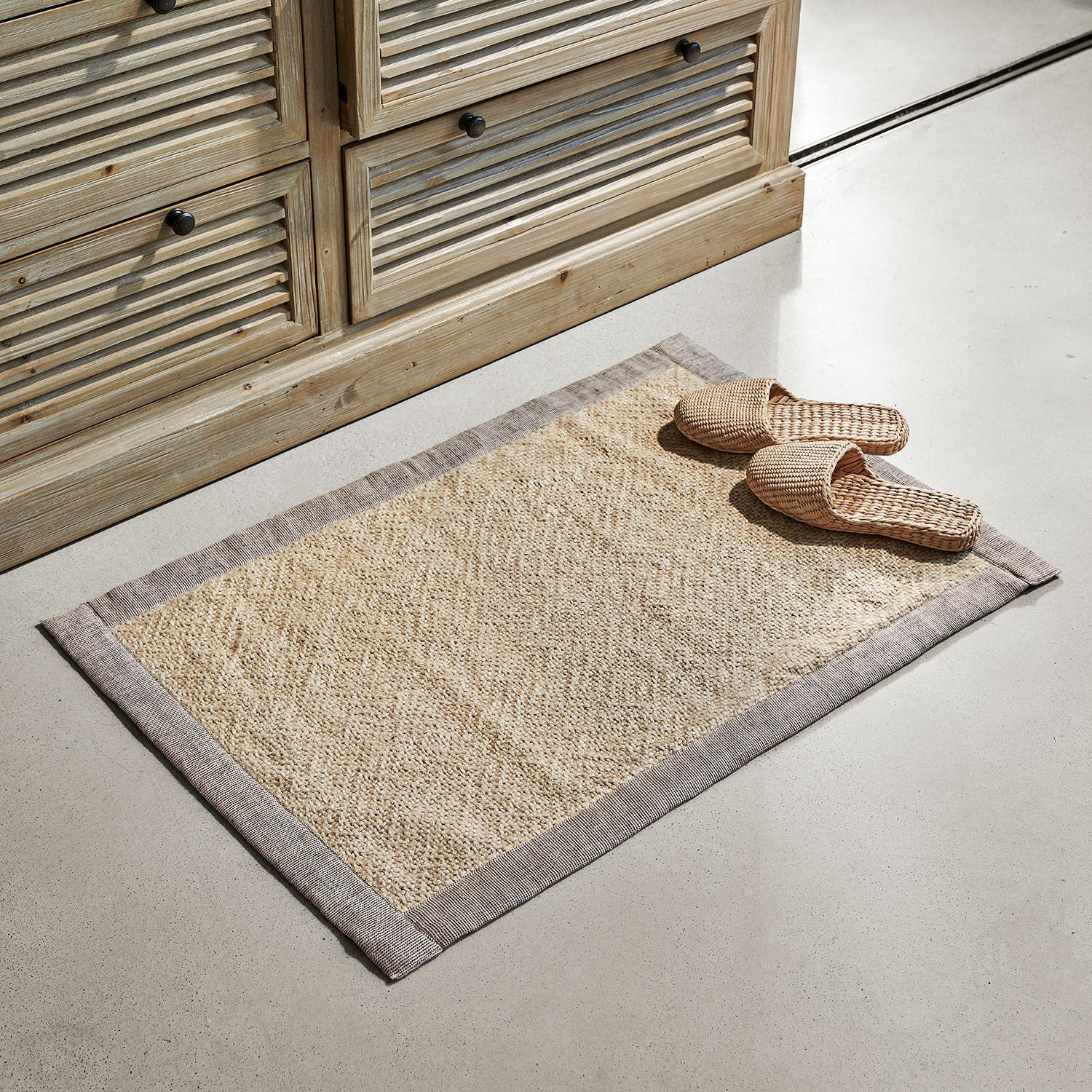 Scendibagno Wilder Tappeto beige in materiale naturale con bordo grigio su pavimento chiaro accanto a mobile in legno