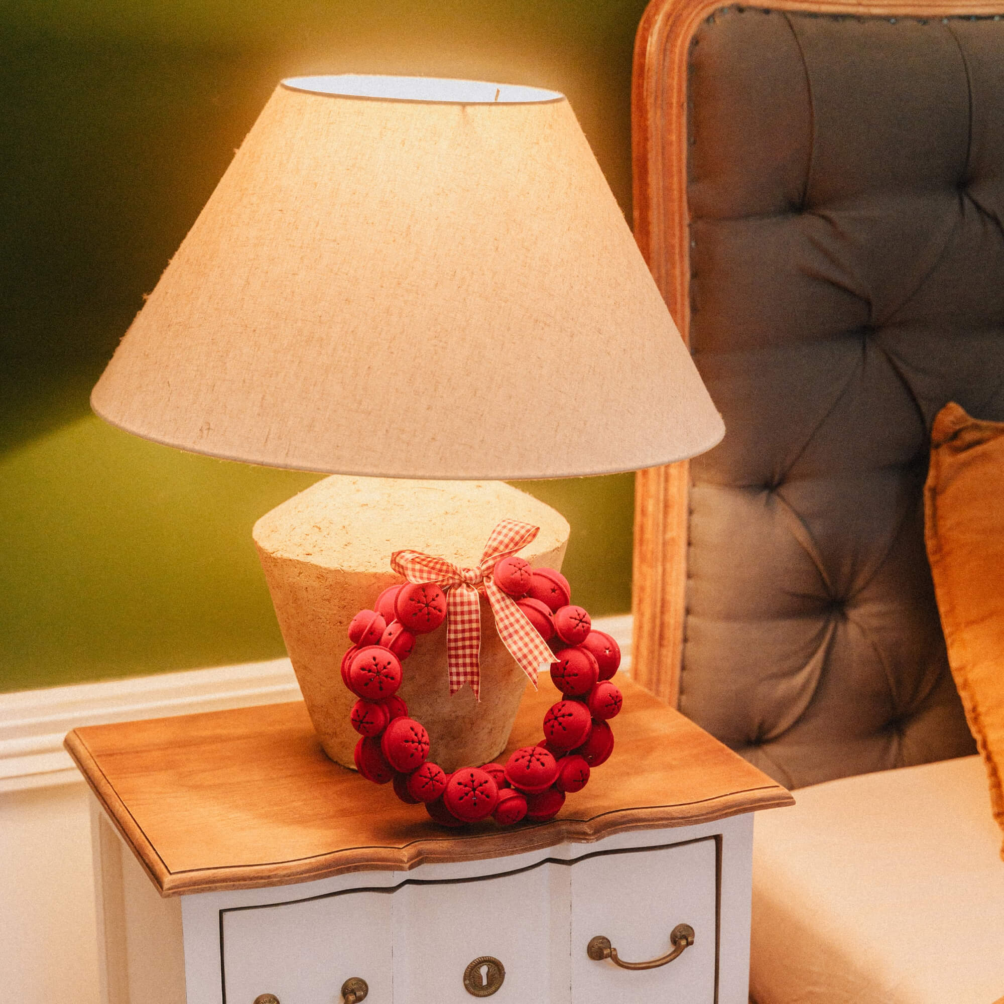 Lampada da tavolo con paralume beige e corona natalizia rossa su comodino in legno