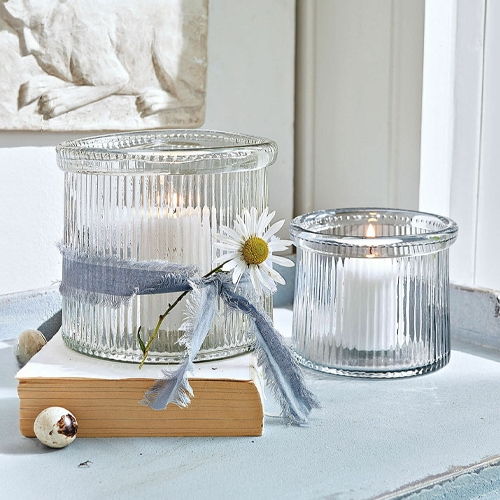Portacandele in vetro rigato con candele bianche e nastro decorativo con fiore bianco.