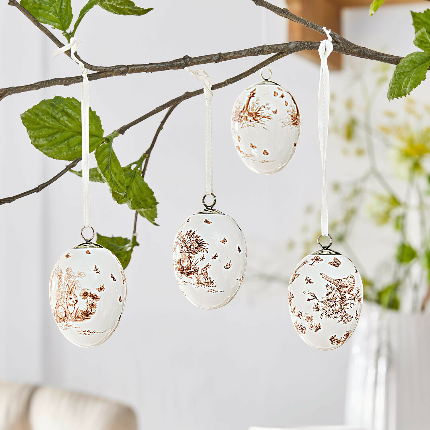 Set di 4 decorazioni da appendere Seravoux Uova di Pasqua in ceramica bianca con motivi marroni di animali e piante appese a un ramo