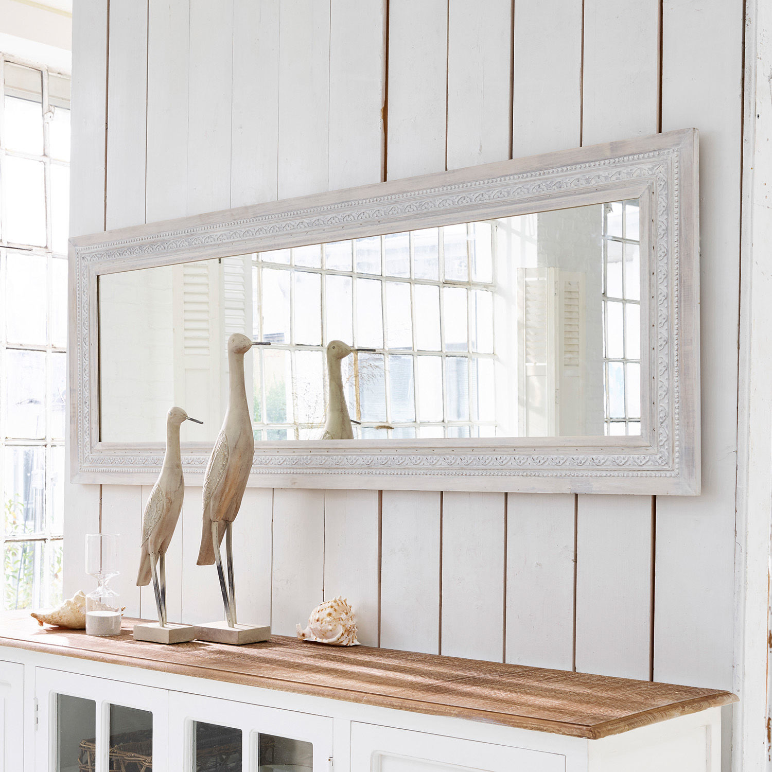 Specchio Milanu Grande specchio rettangolare con cornice in legno bianco sopra un mobile bianco con decorazioni in legno e conchiglie