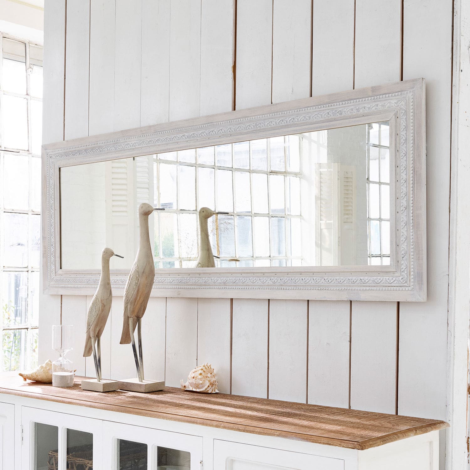 Specchio Milanu Grande specchio rettangolare con cornice in legno bianco sopra un mobile bianco con decorazioni in legno e conchiglie