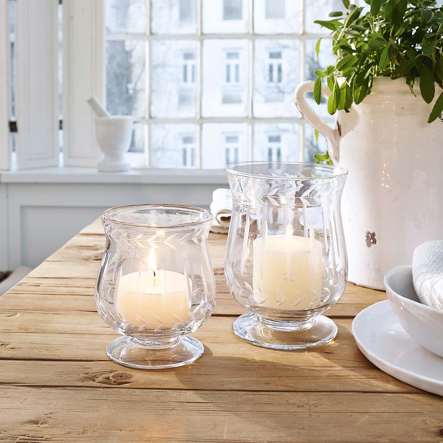 Due portacandele in vetro con candele bianche su tavolo in legno in ambiente luminoso