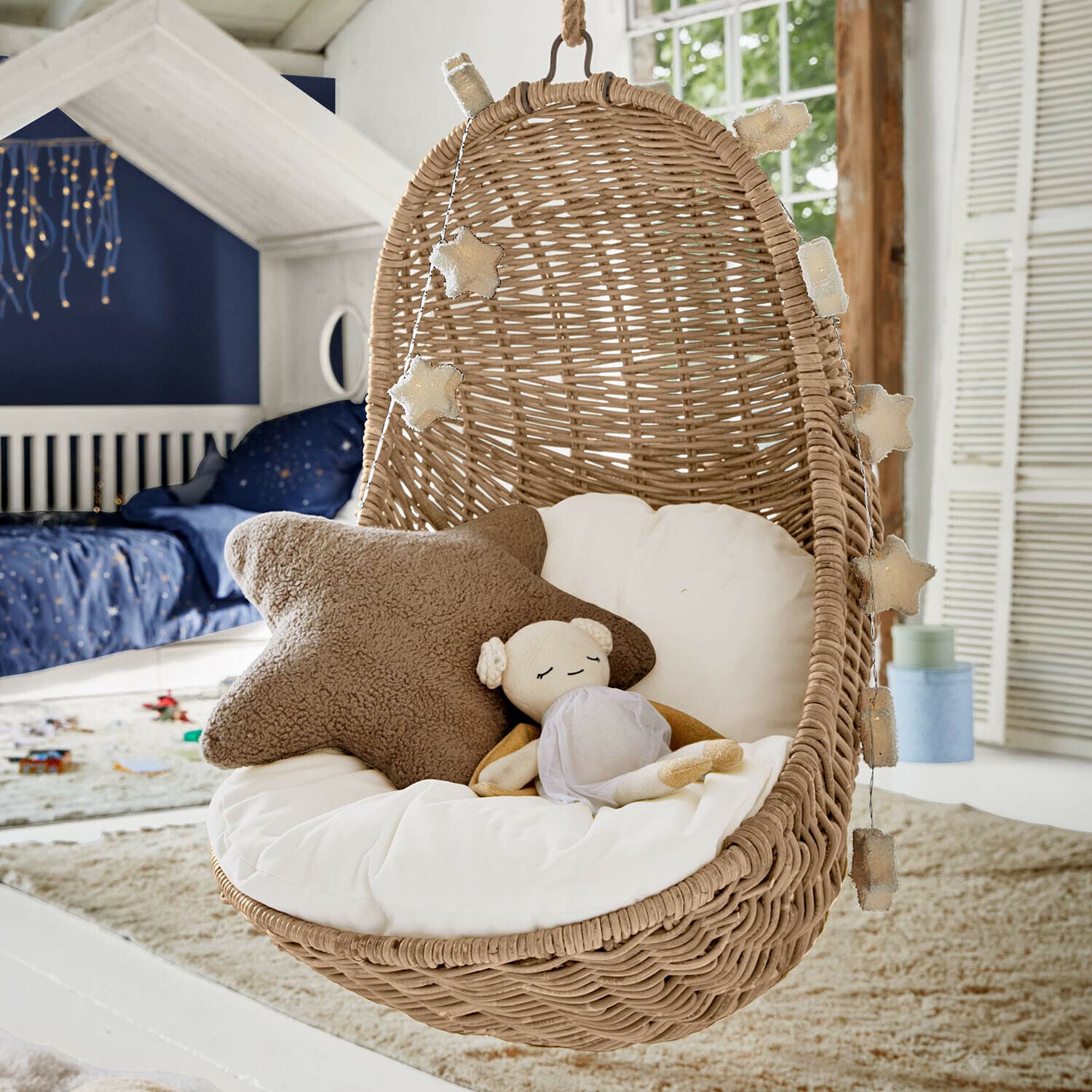 Sedia sospesa in rattan con cuscino bianco e luci a forma di stella in camera per bambini