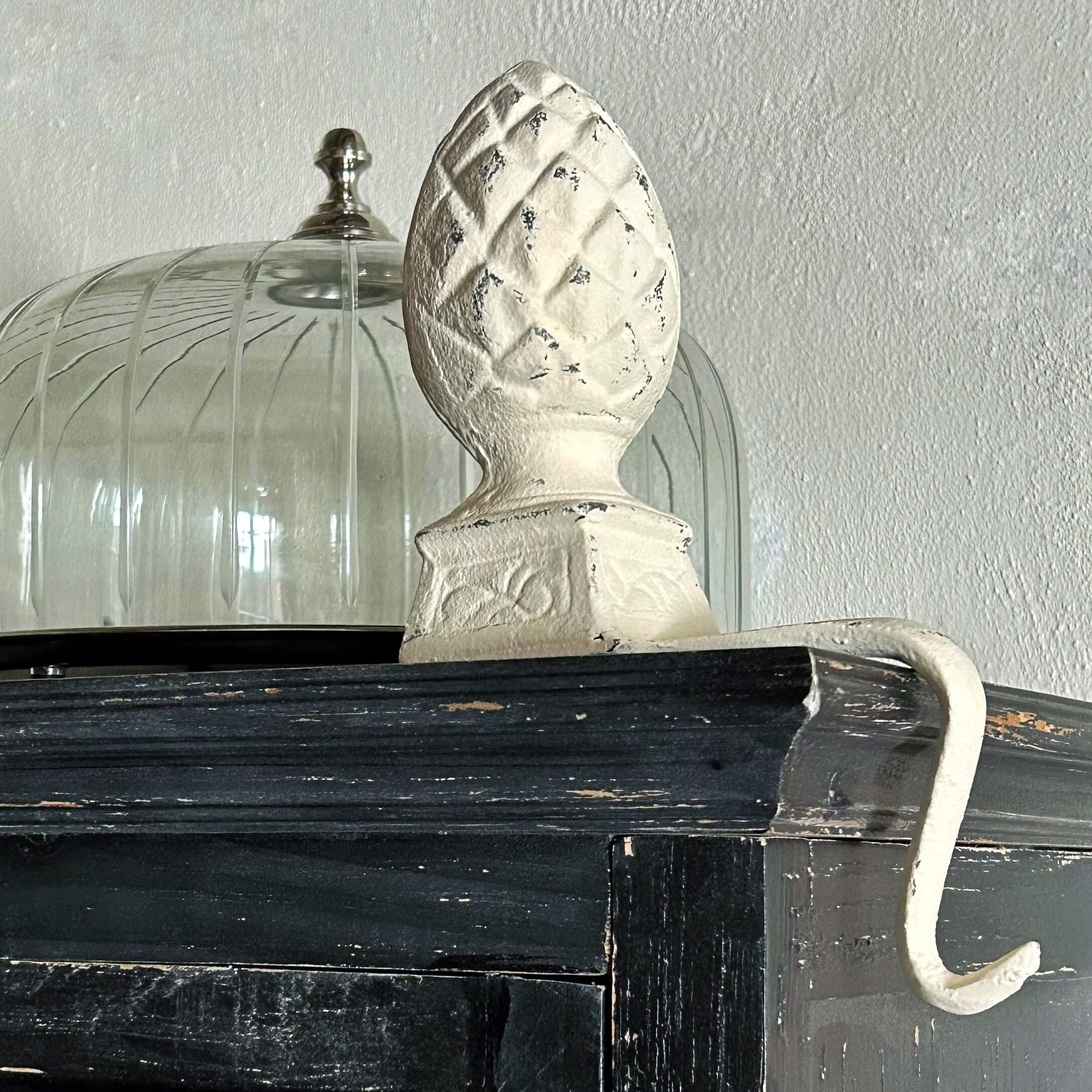 Gancio in metallo bianco con cima decorativa a forma di pigna su mensola in legno nero