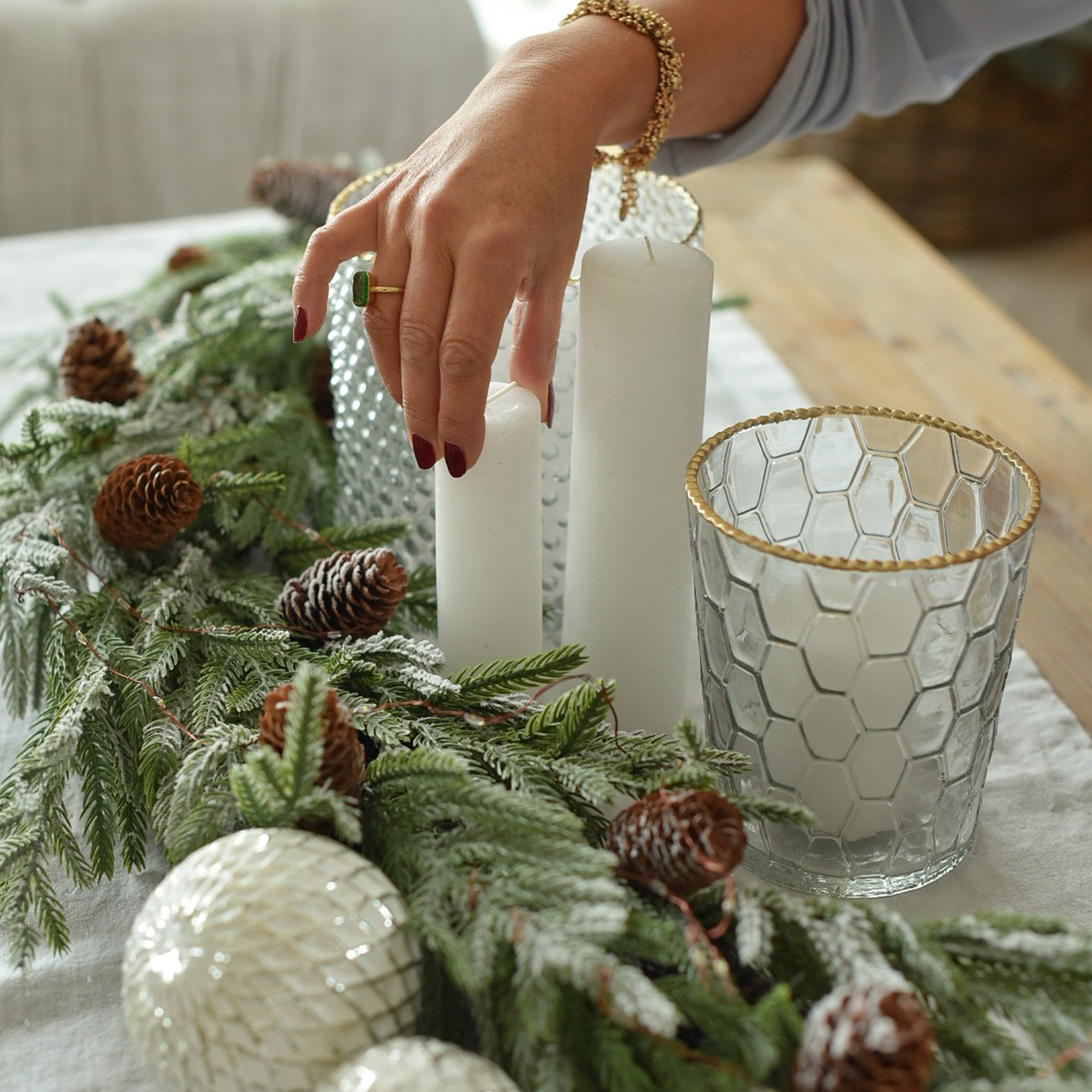 Decorazione natalizia con candele bianche, portacandele in vetro con bordo dorato e rami verdi con pigne