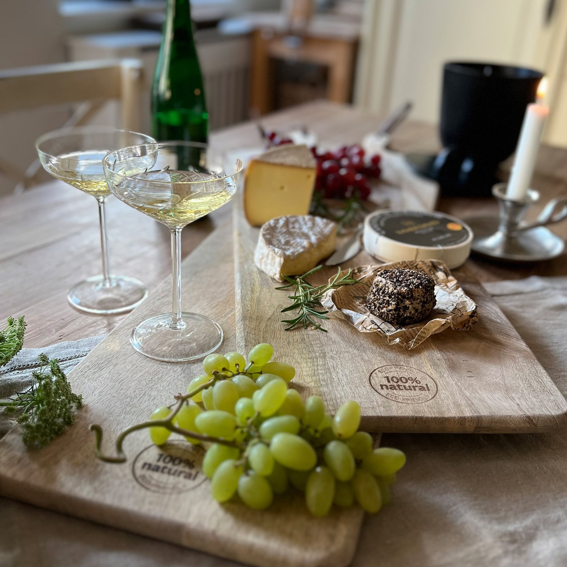Tagliere in legno naturale con uva, formaggi assortiti e bicchieri di vino su tavolo in legno