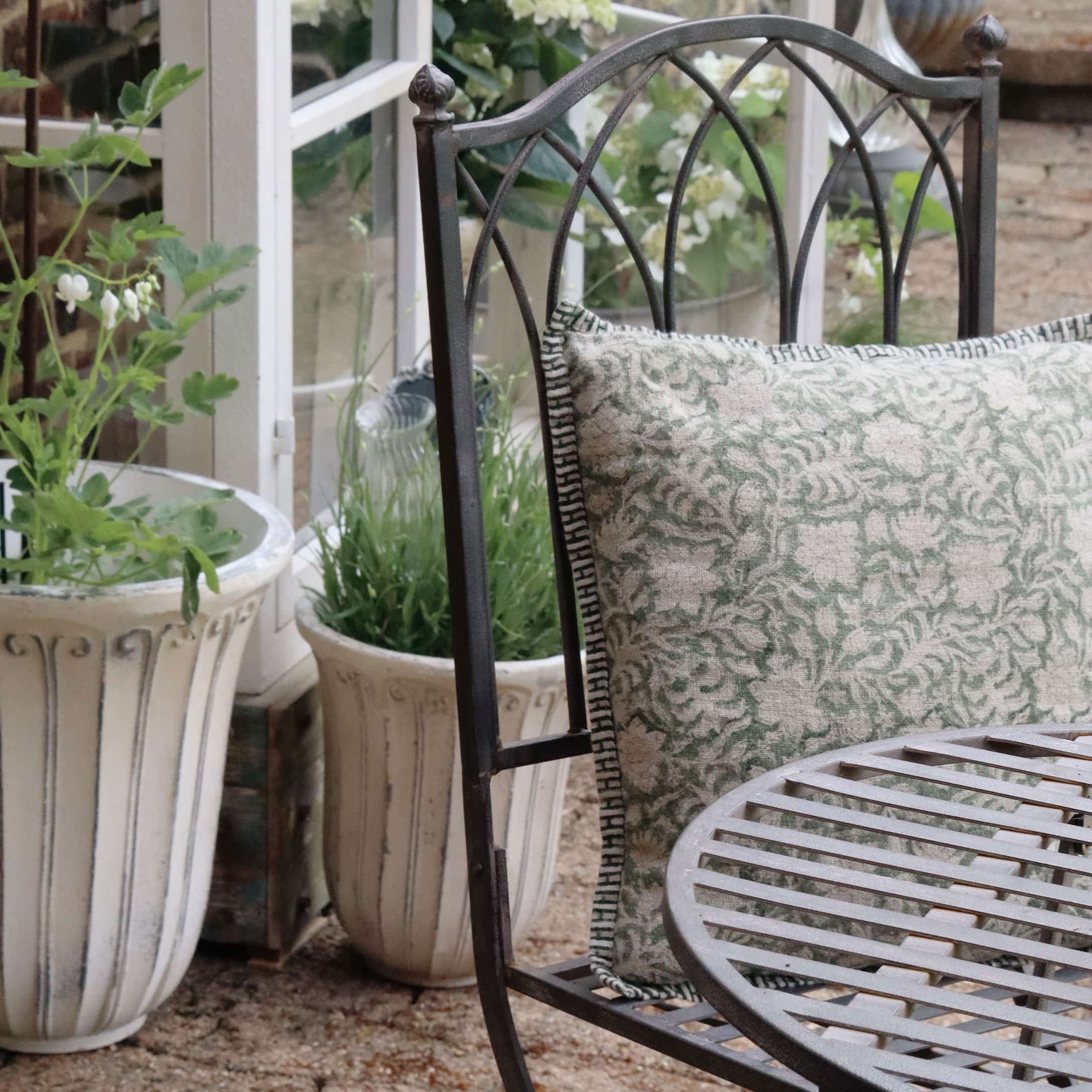 Sedia da giardino in metallo con cuscino verde e beige, circondata da vasi decorativi con piante