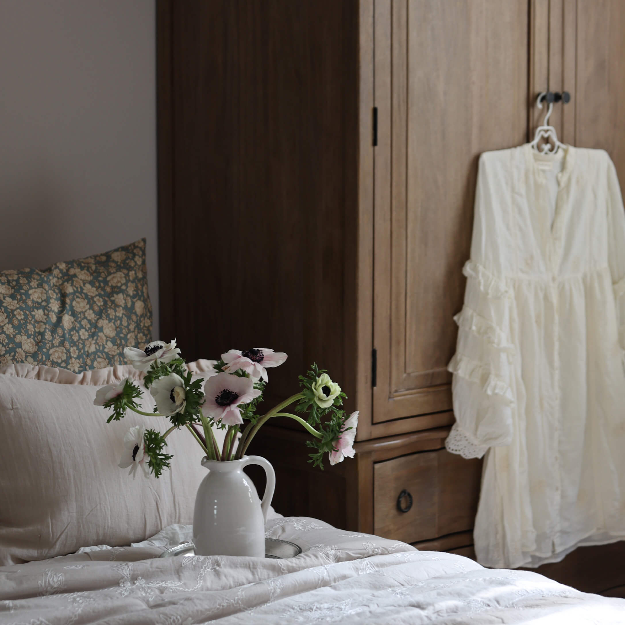 Brocca in ceramica bianca con fiori su letto chiaro davanti a un armadio in legno