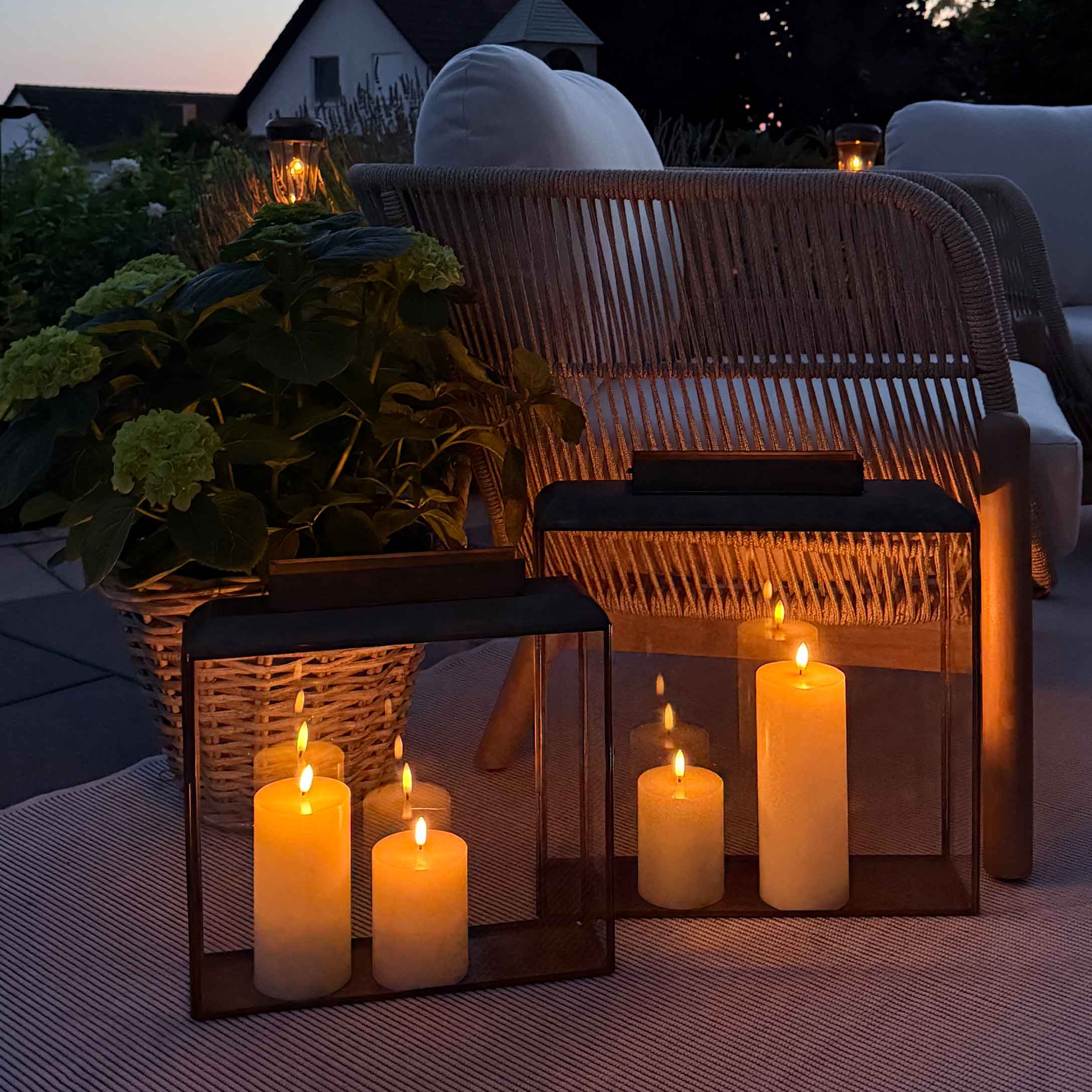Illuminazione d'atmosfera con lanterne e candele su terrazza con poltrona in vimini e cuscino bianco