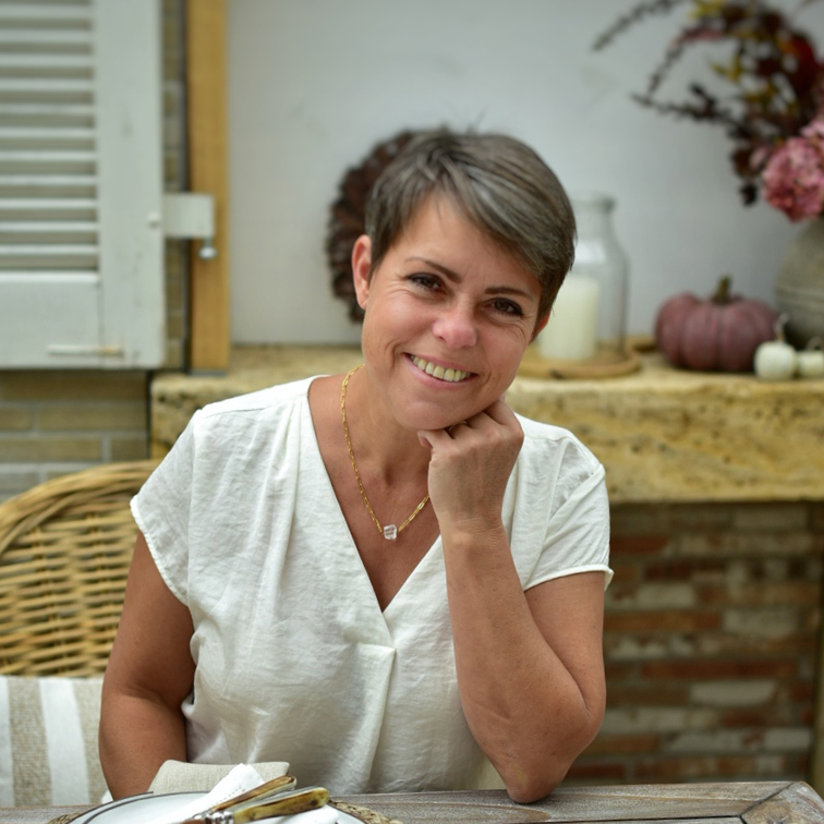 Donna sorridente con camicia bianca seduta a tavola con decorazioni autunnali sullo sfondo