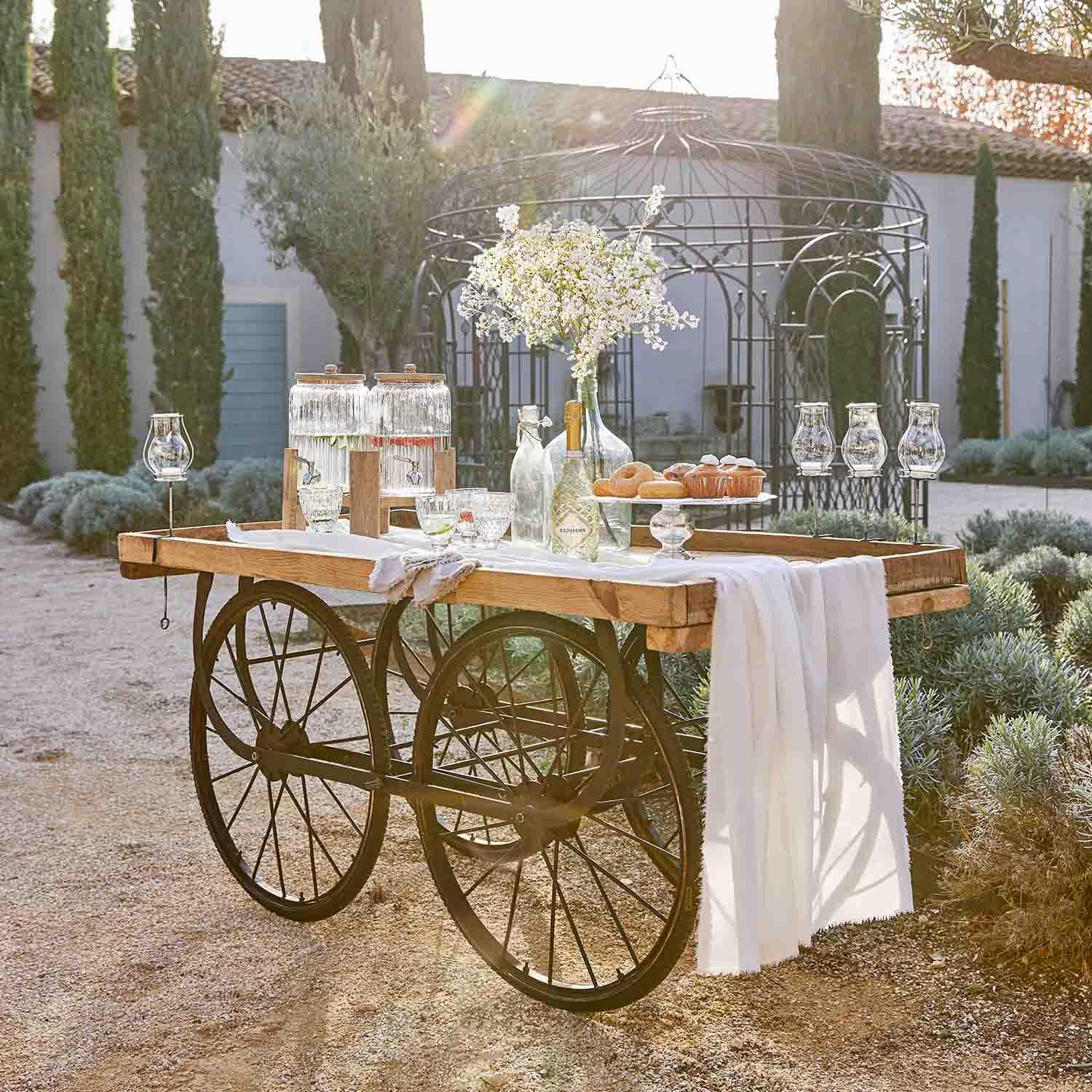 Carretto in legno con ruote in metallo decorato con brocche di vetro e fiori in un giardino soleggiato
