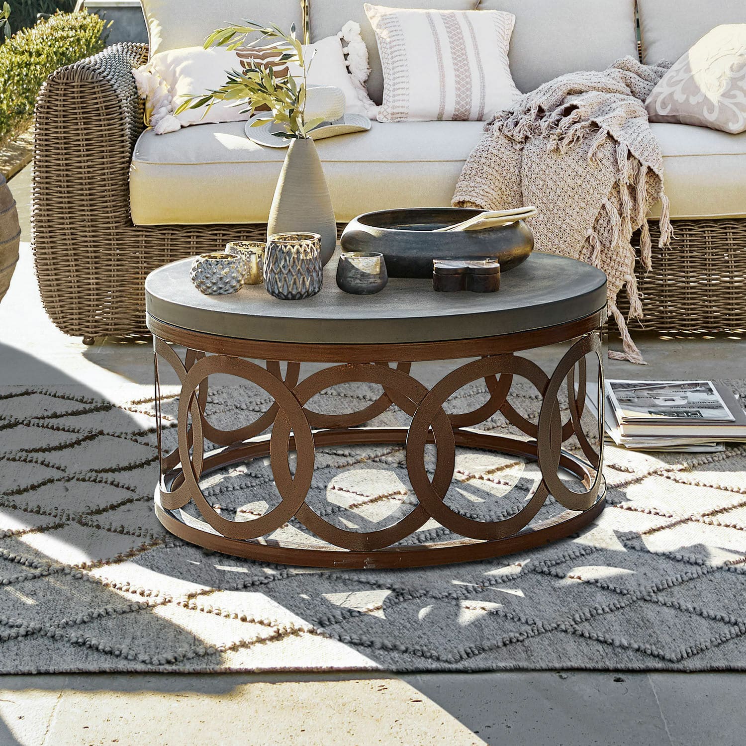 Tavolino da salotto Boécourt Tavolino rotondo con base in metallo arrugginito e piano grigio su terrazza con divano in vimini beige