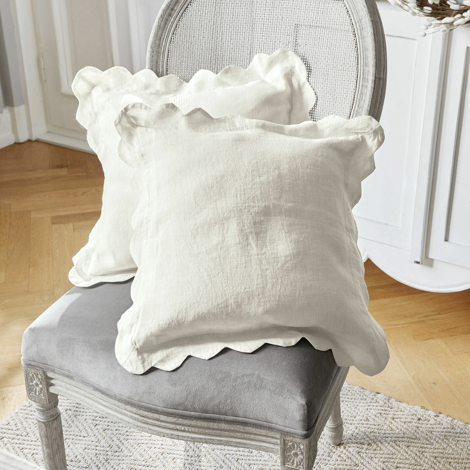Coppia di copricuscini Fontienne Cuscini decorativi in lino bianco con bordo ondulato su sedia imbottita grigia in soggiorno
