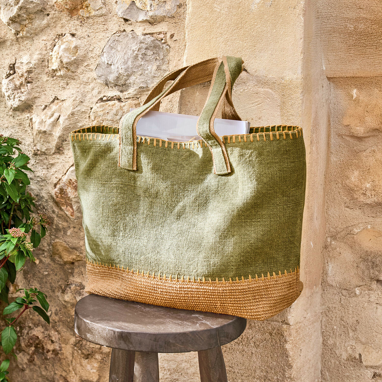 Borsa Yarrowton Borsa verde in juta con rifiniture marroni su uno sgabello di legno vicino a un muro di pietra