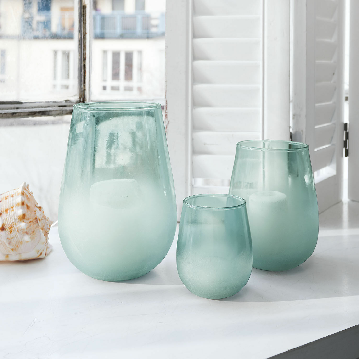 Set di 3 portacandele Miristelle Set di tre portacandele in vetro smerigliato verde su davanzale bianco con candele bianche