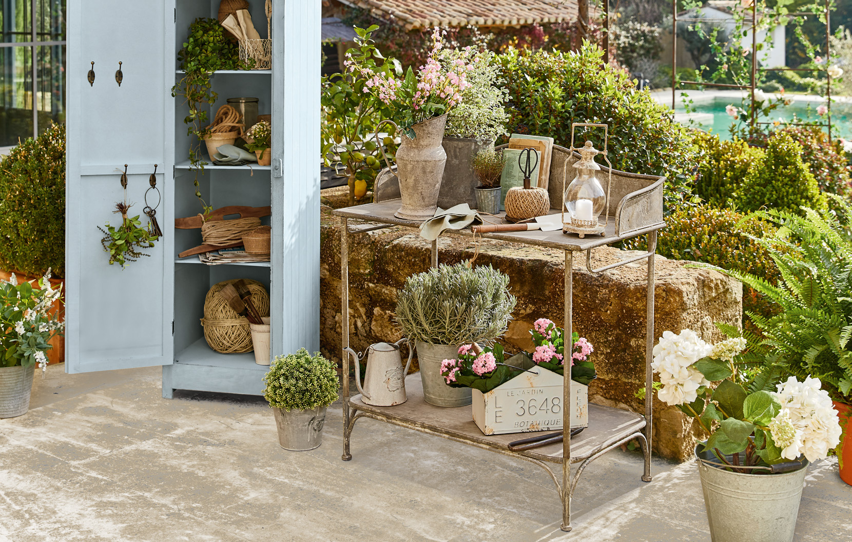 Carrello da giardino in metallo con decorazioni shabby chic e fiori su patio con armadio blu.