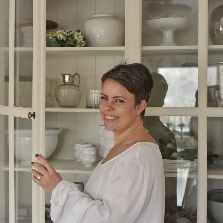 Donna con camicetta bianca apre armadio crema con porcellane e decorazioni in casa