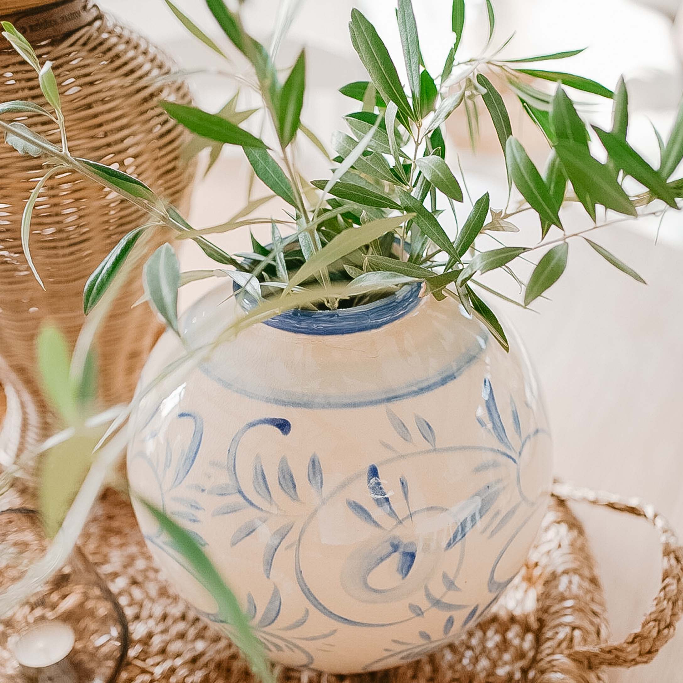 Vaso in ceramica bianca con motivo blu e foglie verdi su vassoio intrecciato, decorazione primaverile