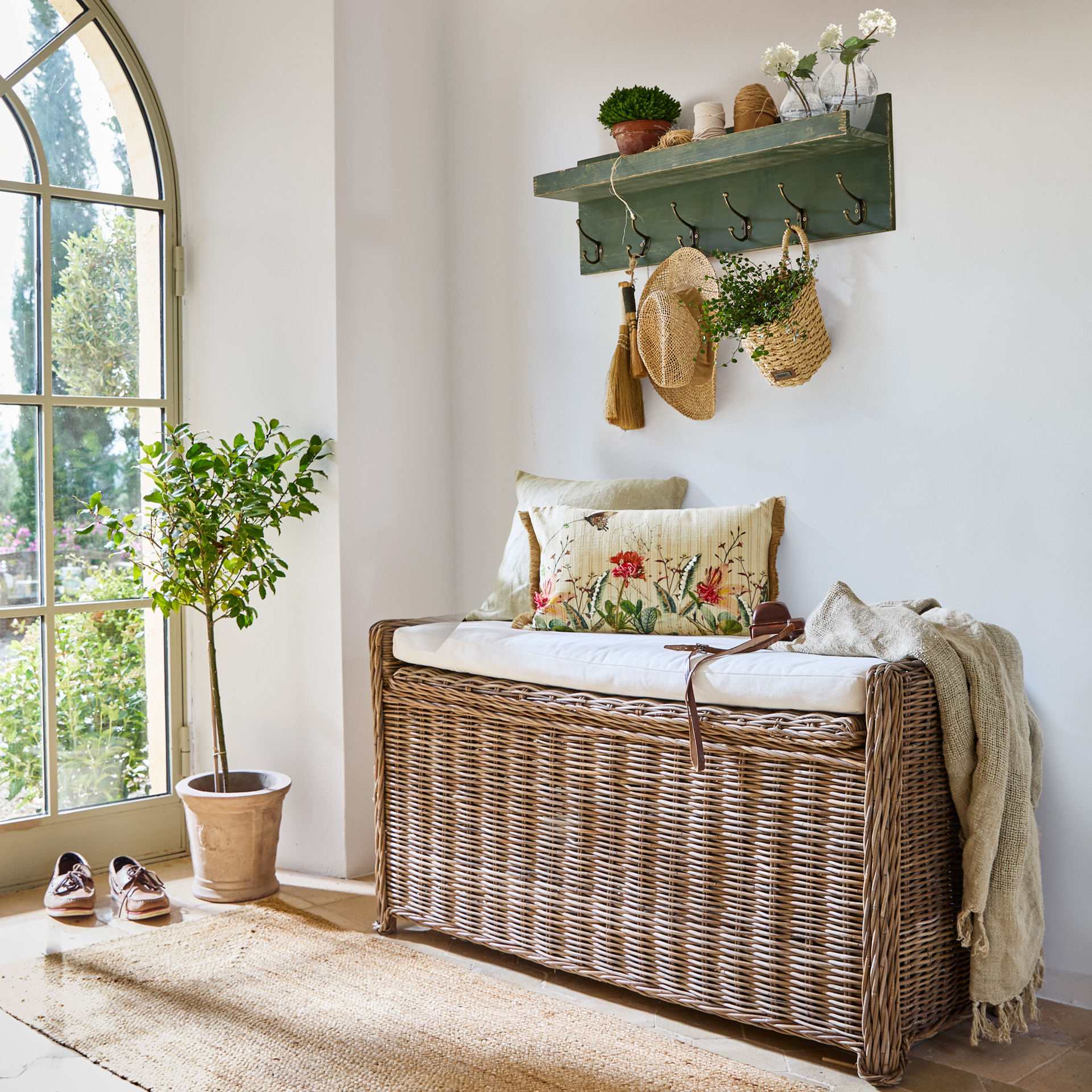 Panca in rattan con cuscino bianco e cuscini decorativi in interno luminoso con appendiabiti verde