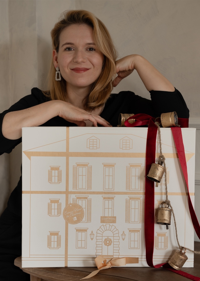 Donna con scatola regalo bianca decorata con disegno dorato di casa e campane rosse per Natale