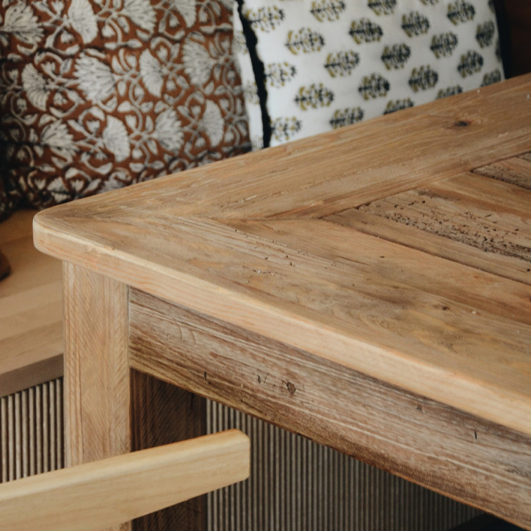 Tavolo in legno chiaro dallo stile rustico con cuscini decorativi sullo sfondo, mobili per soggiorno